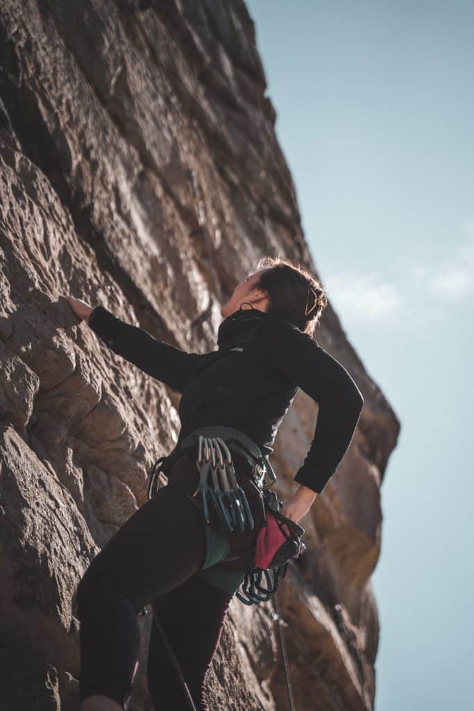 A person lead climbing outside with a blue sky.